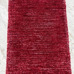 Könnte beinhalten: Ein rechteckiger, plüschiger Teppich in tiefroter Farbe. Der Teppich hat eine strukturierte, zottelige Oberfläche mit horizontalen Linien, die ein weiches und einladendes Aussehen erzeugt. Der Teppich ist für den Innenbereich konzipiert.