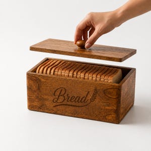 May include: A rectangular wooden bread box with a dark brown finish and a matching lid featuring a small round knob. The front of the box is engraved with the word Bread in a cursive script next to a wheat stalk icon, filled with sliced bread.
