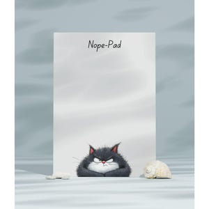 May include: A white notepad with the text "Nope-Pad" is displayed. A grumpy, cartoon black cat with a white chest and a red nose is at the bottom of the notepad. A seashell and a small white stone are on the surface.
