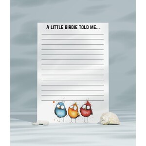 May include: A notepad with the text "A LITTLE BIRDIE TOLD ME..." and lined pages. Below the text are three cartoon birds in blue, orange, and red. A seashell and a small white stone are on the surface.