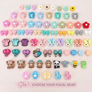 May include: A collection of colorful focal beads in various shapes, including flowers, bows, teddy bears, and scrubs. The beads are in shades of pink, blue, yellow, and green. The text at the bottom says "Step 1: CHOOSE YOUR FOCAL BEAD."