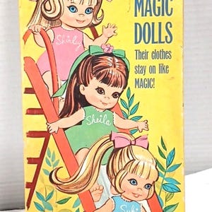 May include: A rectangular yellow cardboard box for Skediddle Kiddles 3 Magic Dolls by Whitman. The box features illustrations of three dolls named Shirley, Sheila, and Suki on a red slide, with text stating, Their clothes stay on like MAGIC!