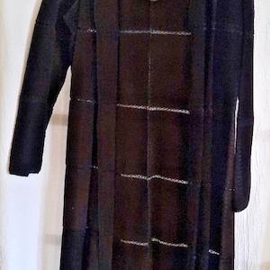 May include: A long, black open-front cardigan with a grid pattern. The cardigan is hanging on a white hanger against a white background. A tag is attached to the cardigan.