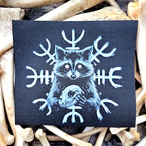 May include: A black square patch featuring a raccoon holding a skull, surrounded by white rune-like symbols. The raccoon is depicted in shades of blue and white. The patch is set against a background of bones.