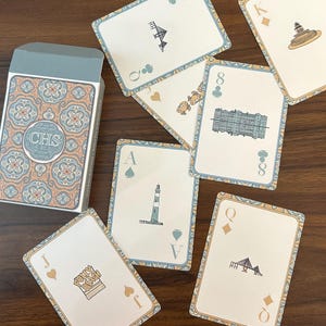 Puede incluir: Una baraja de cartas con una caja decorativa. Las cartas presentan ilustraciones de monumentos y símbolos, con un borde azul y dorado. La caja tiene un estampado floral y las letras "CHS".