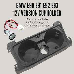 May include: A black 12V version cupholder for BMW E90, E91, E92, and E93 models. The cupholder has two large circular openings and a smaller one. The image also shows a 12V socket and wiring. The text on the cupholder reads "BMW".