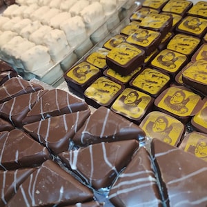 Peut inclure: Présentation de chocolats assortis. Rangées de douceurs enrobées de blanc, chocolats carrés avec motifs jaunes et noirs, et morceaux de chocolat triangulaires rayés de blanc.