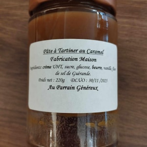 Puede incluir: Un tarro de vidrio con tapa color cobre lleno de crema de caramelo. El tarro tiene una etiqueta blanca con texto en francés, incluyendo "Pâte à Tartiner au Caramel" y "Fabrication Maison." El peso neto es de 220g.