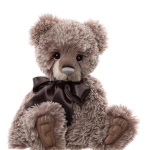May include: A plush teddy bear with soft, textured fur in shades of brown and gray. It features a dark brown satin bow and matching paw pads. The bear has a gray nose and dark eyes, giving it a classic, cuddly appearance.