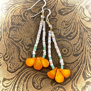 May include: Dangling earrings with white, turquoise, and orange beads. The earrings have silver hooks and feature a cluster of orange teardrop-shaped beads at the bottom. The beads are strung on a thin, beige cord.
