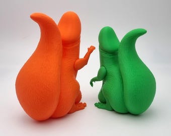 May include: Two quirky dinosaur figurines, one orange and one green. These 3D-printed models feature a distinctive design with a curved tail and small arms. They are set against a white backdrop. The orange dinosaur is raising its arm.