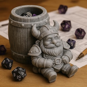 Peut inclure: Un porte-dés en résine grise en forme de tonneau, avec une figurine de nain souriant. Le nain porte un casque à cornes et une armure. Plusieurs dés noirs et violets sont éparpillés autour du support, avec un stylo en bois et du papier en arrière-plan.