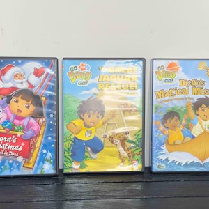 May include: Three children's DVDs featuring Dora the Explorer and Go, Diego, Go! The DVDs include "Dora's Christmas", "The Great Jaguar Rescue", and "Diego's Magical Missions". Each DVD case has colorful illustrations of the characters.
