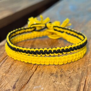 May include: A yellow and black friendship bracelet with a braided design. The bracelet is made of two strands of string, one yellow and one black, that are woven together.