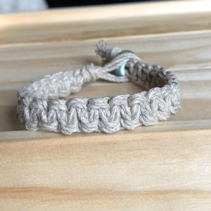 May include: A beige braided bracelet with a light blue bead accent.