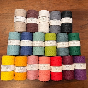 May include: A collection of 20 spools of hemp cord in various colours, including natural, brown, white, grey, black, blue, green, yellow, orange, pink, red, purple, and burgundy. Each spool is labelled "Hemp Cord" with the brand name "Champagne" and the size "3/16".