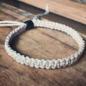 Op de afbeelding: Een wit gevlochten touw armband met een zwarte kraal accent.