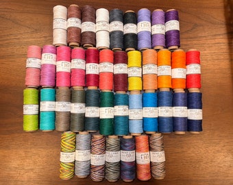 Puede incluir: Una colección de 30 carretes de cuerda de cáñamo en varios colores, incluyendo rojo, azul, verde, amarillo y naranja. Cada carrete está etiquetado con "Hemp Cord" y tiene un número.