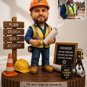 May include: A custom bobblehead figurine of an engineer wearing an orange hard hat, blue shirt, and high-visibility vest, holding a blueprint and pen. The base features a wooden sign with text, a traffic cone, a mug, and a small surveyor tripod.