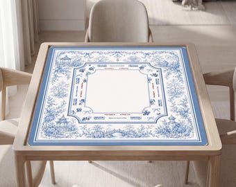 Puede incluir: Un tapete cuadrado para mesa de mahjong con un patrón toile de jouy en azul y blanco que muestra paisajes, pagodas y puentes. El centro incluye instrucciones de juego impresas y marcadores direccionales, rodeados por un borde decorativo.