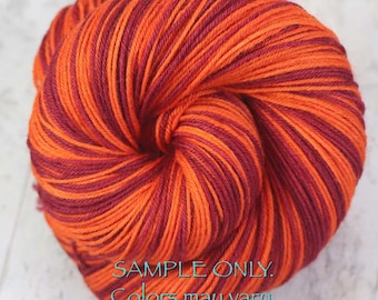 Könnte beinhalten: Ein rundes Garnknäuel mit einem bunten Farbmuster aus leuchtend orangefarbenen und dunkelburgunderroten Strängen, die miteinander verzwirnt sind. Der Text SAMPLE ONLY. Colors may vary due to fiber content. steht in Türkis unten auf dem Garn.