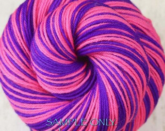 Könnte beinhalten: Ein rundes Garnknäuel mit abwechselnden Strängen in leuchtendem Pink und tiefem Violett. Das Garn ist zu einer festen, kreisförmigen Spule gewickelt. Der Text unten im Bild lautet: SAMPLE ONLY. Colors may vary due to fiber content.