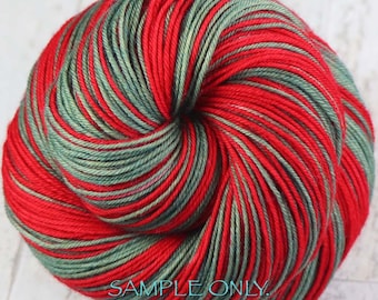 Könnte beinhalten: Ein rundes Garnknäuel mit einem melierten Muster aus leuchtend roten und gedämpften salbeigrünen Fasern, die miteinander verzwirnt sind. Der Text SAMPLE ONLY. Colors may vary due to fiber content. ist in Türkis auf dem unteren Teil zu sehen.