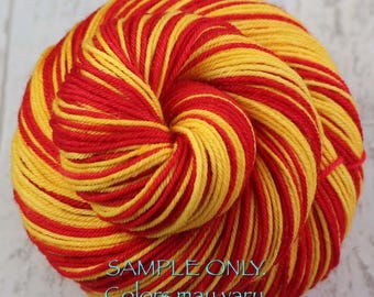 Könnte beinhalten: Ein rundes Garnknäuel mit abwechselnden Strängen in leuchtendem Rot und Gelb. Das Garn ist in einem engen, kreisförmigen Muster gewickelt. Der Text am unteren Bildrand lautet: SAMPLE ONLY. Colors may vary due to fiber content.