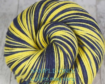 May include: A skein of yarn with alternating stripes of yellow and navy blue. The yarn is tightly wound, with the text "SAMPLE ONLY Colors may vary due to fiber content" in the lower portion of the image.