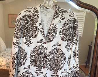 May include: A white long-sleeved button-up shirt with a brown paisley print. The shirt has a collar and a button closure.