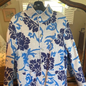 May include: A white quilted jacket with a blue and navy floral pattern. The jacket has a mandarin collar, a button closure, and two pockets.