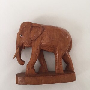 May include: A wooden elephant figurine with a brown finish. The elephant is standing on a wooden base and has a long trunk.