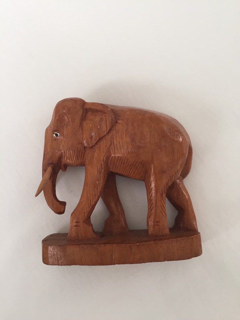 May include: A wooden elephant figurine with a brown finish. The elephant is standing on a wooden base and has a long trunk.