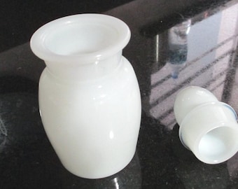 May include: White ceramic bottle with a white ceramic lid. The bottle has a round body and a wide mouth. The lid has a smooth, rounded top.