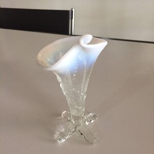 May include: A white iridescent glass vase with a flared opening and a delicate, clear glass base with a four-pronged design.
