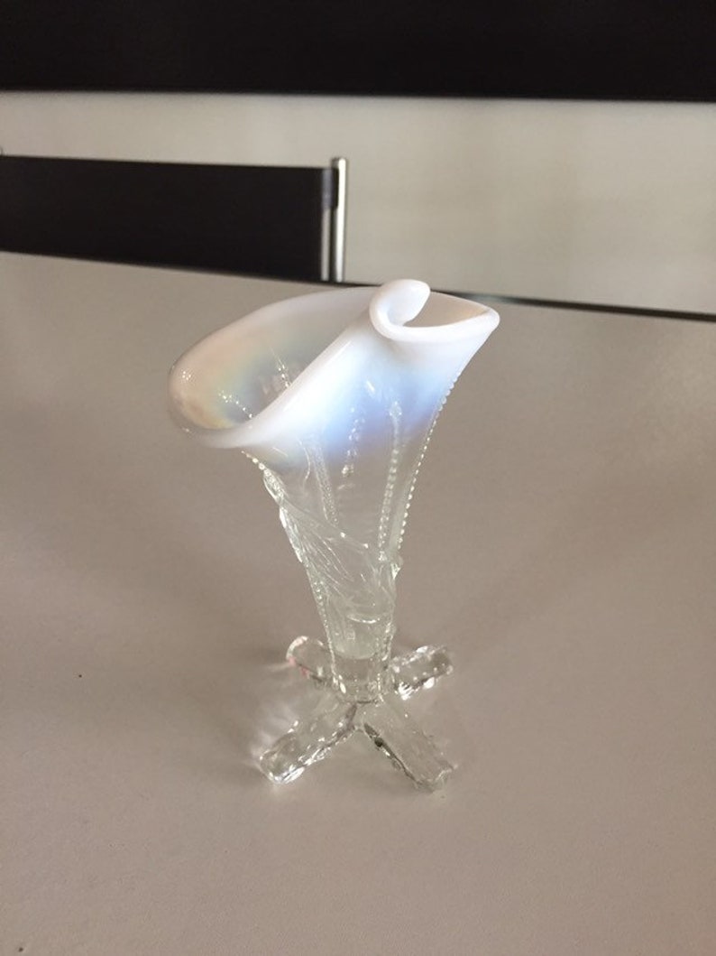 May include: A white iridescent glass vase with a flared opening and a delicate, clear glass base with a four-pronged design.