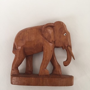 May include: A wooden elephant figurine with a brown finish. The elephant is walking with its trunk raised and has a small white dot for an eye.