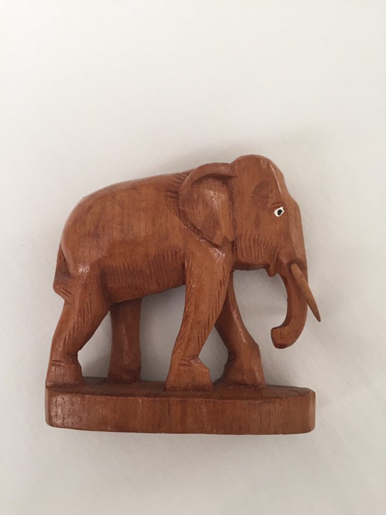 May include: A wooden elephant figurine with a brown finish. The elephant is walking with its trunk raised and has a small white dot for an eye.