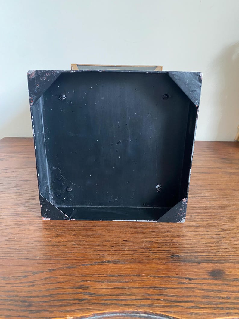 K&ouml;nnte beinhalten: Eine schwarze Metallbox mit rechteckiger Form. Die Box weist eine leicht abgenutzte Optik mit sichtbaren Abnutzungserscheinungen an den Ecken auf. Der Innenraum ist ebenfalls schwarz, und die Box steht auf einer Holzoberfl&auml;che.