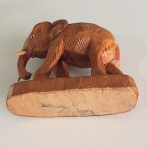 May include: A wooden elephant figurine with a brown finish. The elephant is standing on a wooden base with the text "Made in India" on the bottom.