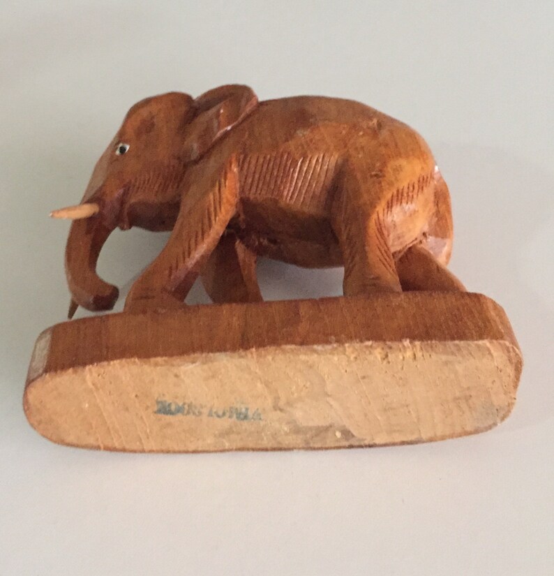 May include: A wooden elephant figurine with a brown finish. The elephant is standing on a wooden base with the text "Made in India" on the bottom.
