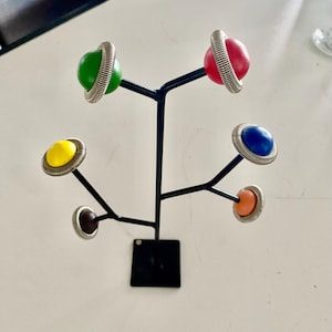 May include: A black metal stand with six colorful round ornaments. The ornaments are attached to the stand with silver rings. The ornaments are yellow, green, red, blue, orange, and brown.