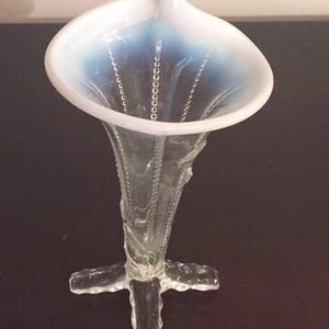 May include: A clear glass vase with a white and blue iridescent finish. The vase has a trumpet-shaped opening and a four-pronged base.