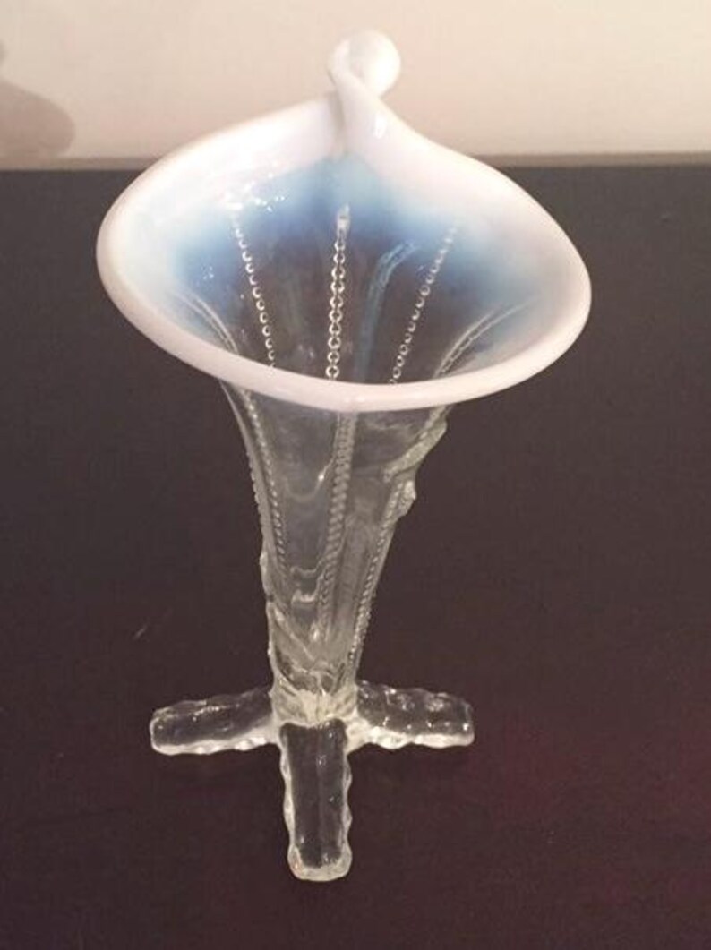May include: A clear glass vase with a white and blue iridescent finish. The vase has a trumpet-shaped opening and a four-pronged base.