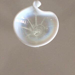 May include: A white iridescent glass dish with a swirl design. The dish has a small handle on the top.