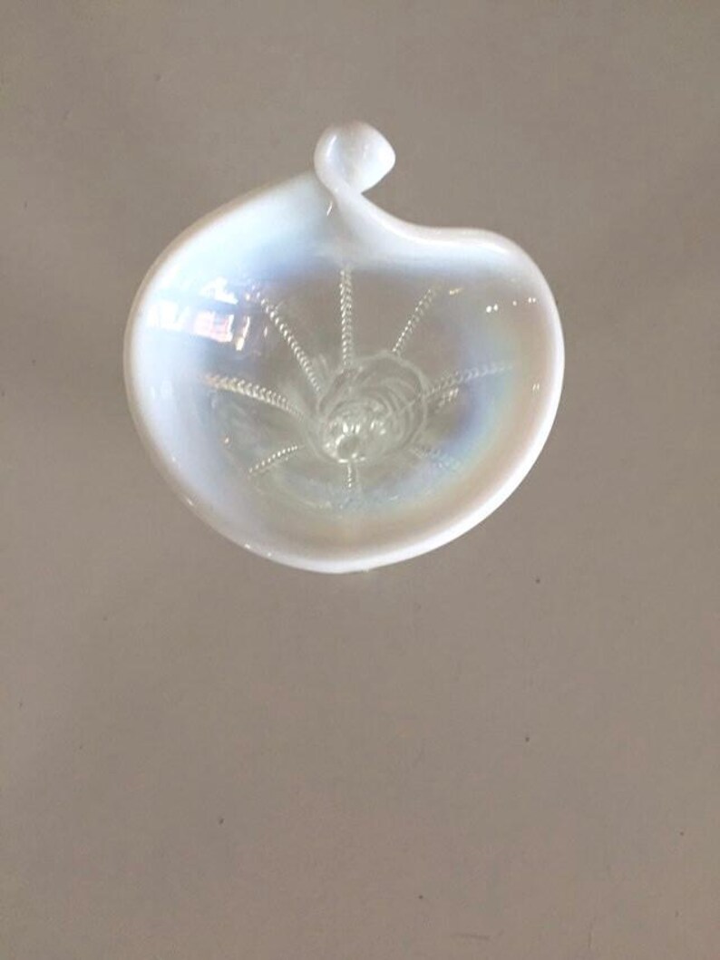 May include: A white iridescent glass dish with a swirl design. The dish has a small handle on the top.
