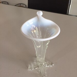May include: A white iridescent glass vase with a trumpet-shaped opening and a delicate, clear glass stem with a four-pronged base.