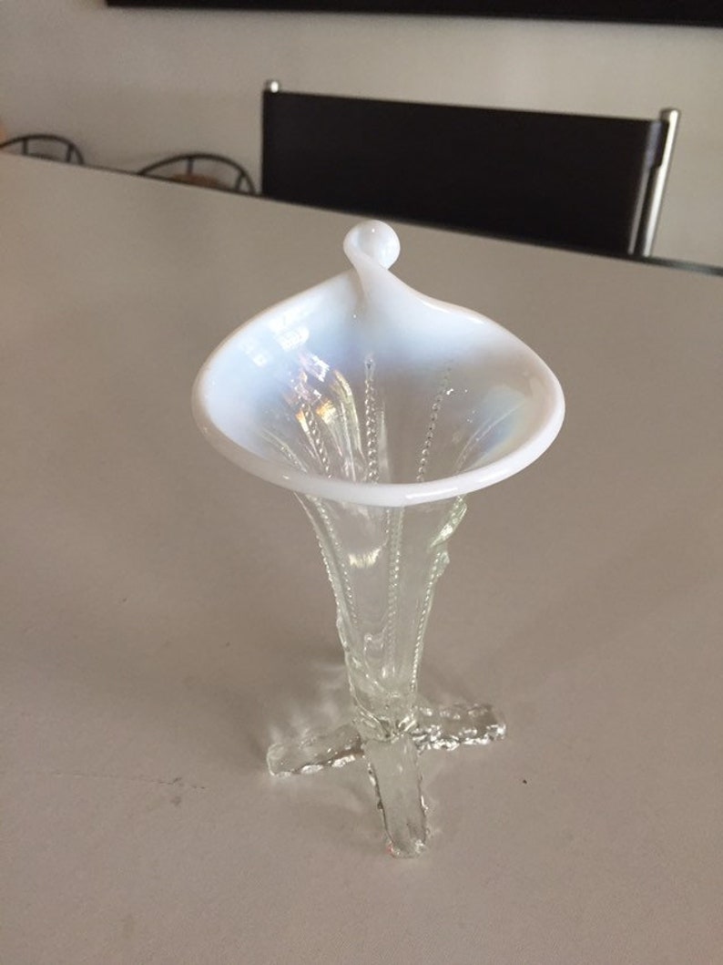 May include: A white iridescent glass vase with a trumpet-shaped opening and a delicate, clear glass stem with a four-pronged base.