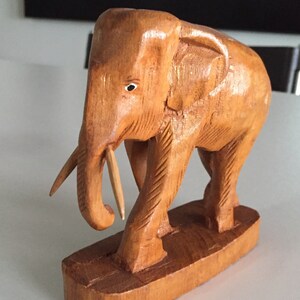 May include: A wooden elephant figurine with a carved trunk and detailed legs. The elephant is standing on a wooden base.
