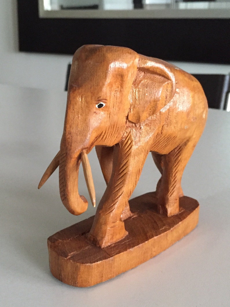May include: A wooden elephant figurine with a carved trunk and detailed legs. The elephant is standing on a wooden base.